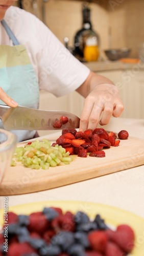 Foto Woman's hands are precisely chopping fresh strawberries and rhubarb on a wooden