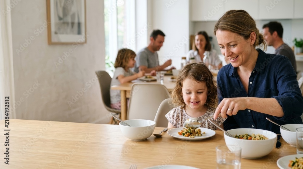 Fototapeta premium Mother lovingly serves food to her daughter at a family dinner, creating a warm, intimate moment in a bright, modern kitchen.