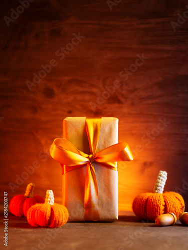 concept of a Thanksgiving gift. A gift box with a gold ribbon and small knitted orange pumpkins, copy space.