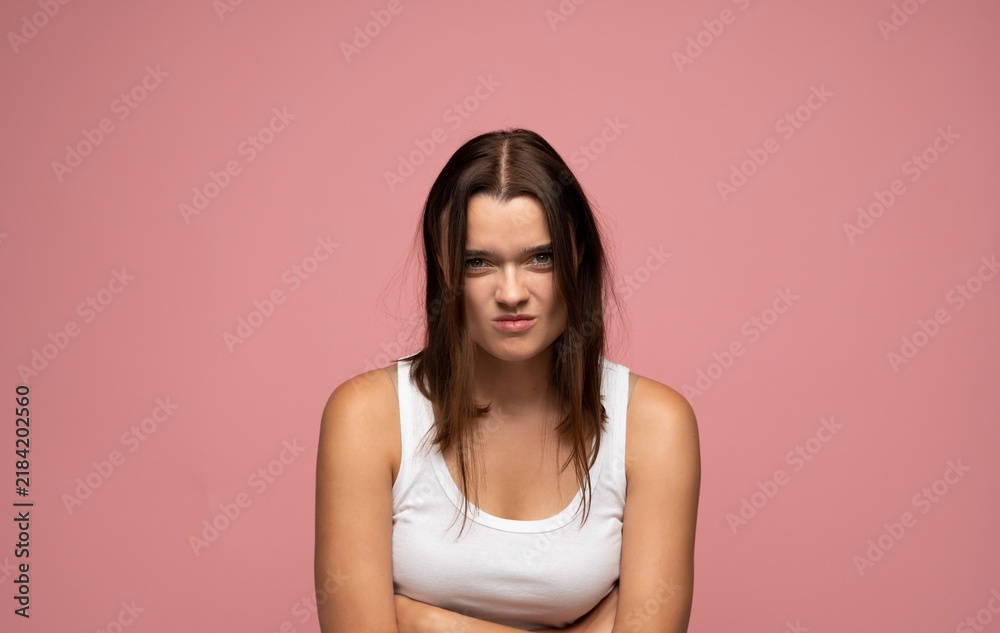 Obraz premium Young woman standing with arms crossed, grumbling on a pink background, expressing irritation and displeasure