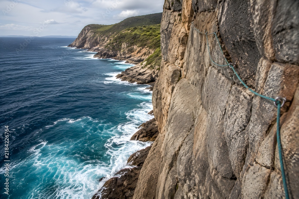 Obraz premium Rock Climbing Route Up Sheer Sea Cliff Above Crashing Waves with Fixed Rope Adventure Challenge
