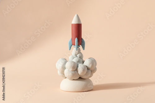 Quadro su tela Handmade clay rocket launching with clouds of smoke on a soft peach background a