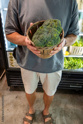 Bild auf Leinwand Solomons, Maryland USA A man at a farm stand hold a bushel of broccoli