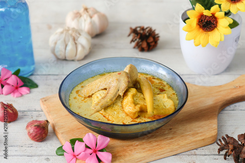 Фотография A bowl of Indonesian chicken curry (kari ayam or kare ayam) featuring a rich coconut milk broth, white tofu, and tender chicken wings, seasoned with aromatic spices such as turmeric and lemongrass