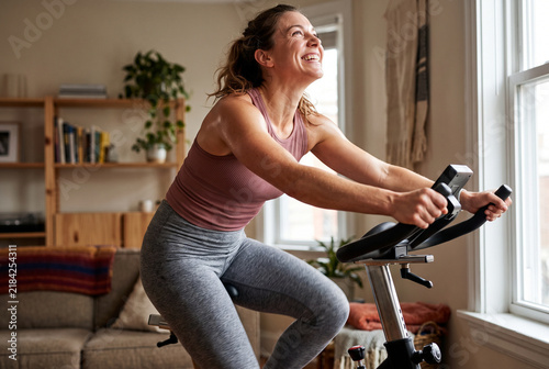 Cheerful Young Woman Celebrating Workout Goal on Indoor Stationary Bike in Sunlit Living Room, Morning Home Fitness Routine