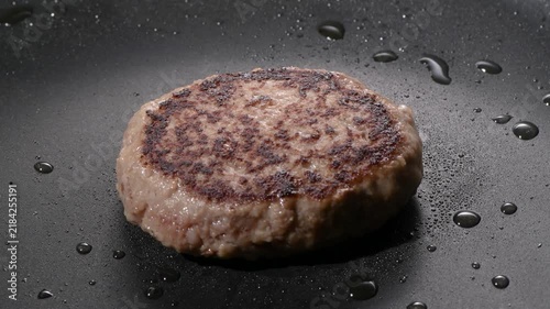Grilled hamburger steak patty with seared crust cooking on a black griddle, camera zooms in and pans across the surface