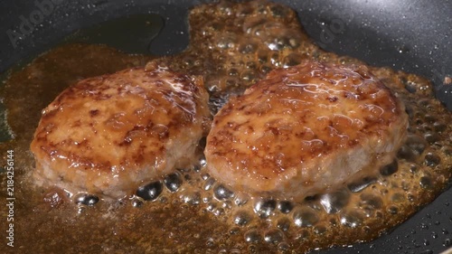 Two raw hamburger steak patties starting to cook on a black frying pan before browning