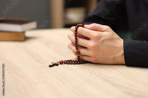 Фотография Priest in cassock with rosary praying at wooden table indoors, closeup