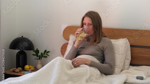 Woman sick in cozy bedroom bed scene holding glass of lemon water in morning wellness mood, with woman, bed, bedroom, interior detail, showing lifestyle, calm, relaxed, morning context