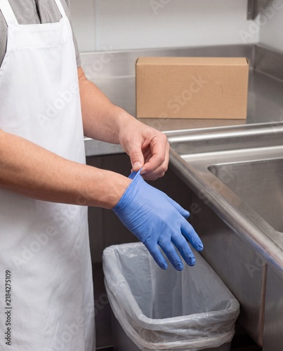Food handler removing disposable glove beside waste bin