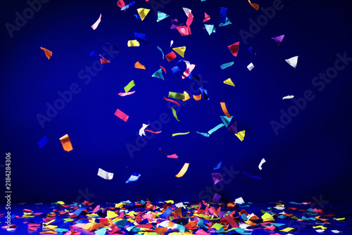 Vibrant multicolored paper confetti raining down against a deep blue surface for a festive holiday celebration party