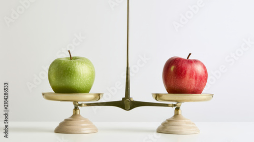 Green apples vs red apples with brass balance scale on white table, nutrition comparison concept