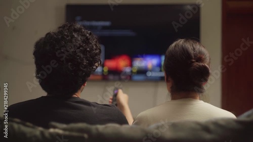Relaxed couple choosing movie from streaming platform on smart TV for date night at home