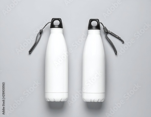Two white, stainless steel water bottles, arranged symmetrically on a grey backdrop
