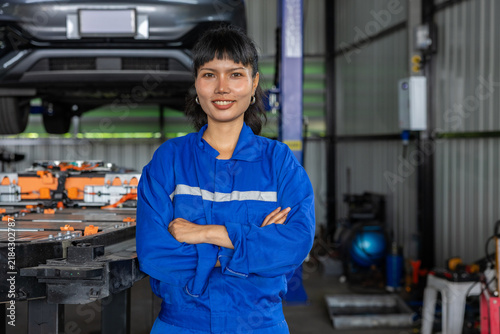 Foto Confident female mechanic in blue coverall standing with crossed arms inside aut