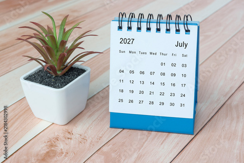 July 2027 desk calendar with potted plant on wooden desk.