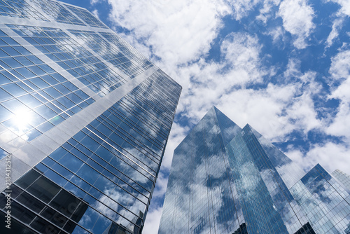 Low angle view of modern glass skyscrapers reflecting a bright blue sky with scattered white clouds. 
