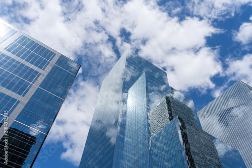 Low angle view of modern glass skyscrapers reflecting a bright blue sky with scattered white clouds. 
