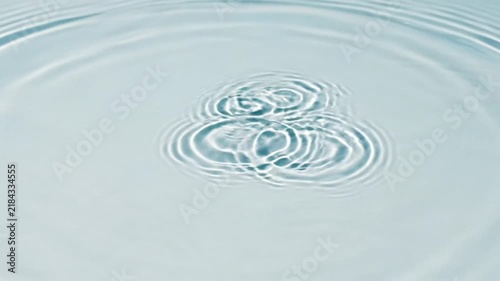 A single clear water drop creates ripples on a calm surface