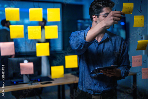 Canvas Print A young male engineer organising a colourful task wall with a tablet in hand tap