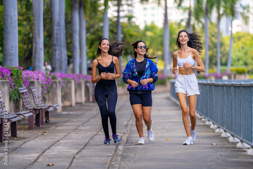 Konstfotografi Three fit female friends in matching activewear, laughing as they run, keep pace with each other on a morning run in matching activewear and running shoes, a fitness concept