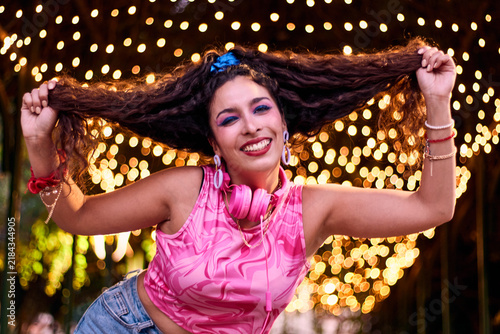 Foto Beautiful, made-up, cheerful woman, straightening her hair, charismatic, dressed in colorful clothes, against a backdrop of lights, outdoors