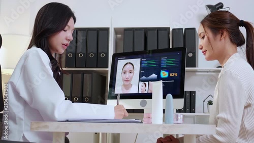 Asian woman doctor explaining ai face skin analysis on computer screen for female patient in clinic while dermatologist writing note on clipboard document, medical healthcare beauty consult.