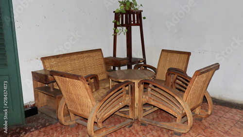 Aesthetic rustic corner room with ancient woven cane chairs round coffee table green plants decoration and old traditional indonesian pattern floor tiles.