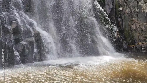 A scenic and powerful waterfall cascades down dark rocky cliffs into a turbulent pool of water in a serene natural forest landscape