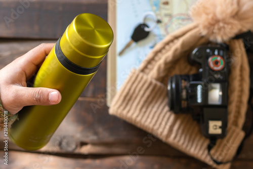 A top-down view of a man's hand holding a metal water bottle and hiking gear on a rustic wooden table
