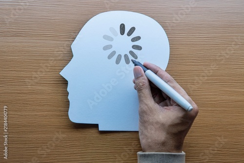 Hand drawing a loading icon onto a white paper human head silhouette. Mental fatigue, brain fog, cognitive delay, slow learning concept.