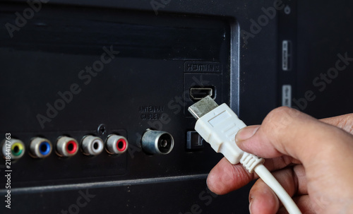 фотографія Close-up of a hand plugging a white HDMI cable into an HDMI port on the back of a television