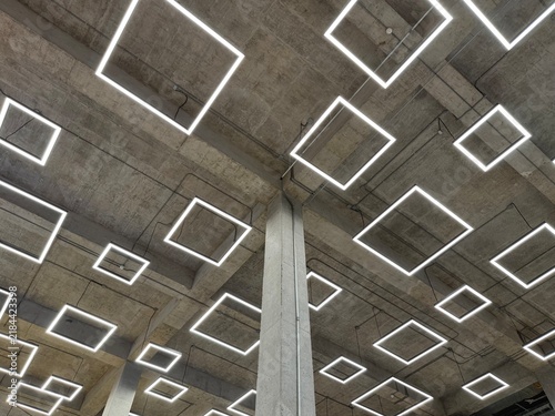 Modern industrial concrete ceiling with hanging square LED pendant lights.