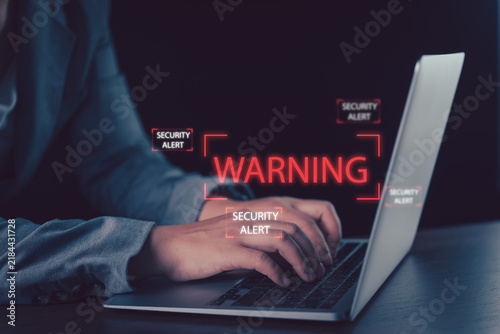 Cybersecurity warning concept featuring a business professional using a laptop with glowing alerts