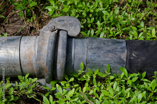 Rusty industrial hose coupling and rubber hose lying on ground, showing wear and heavy use at a construction or irrigation site, evoking maintenance, repair, and outdoor work.
