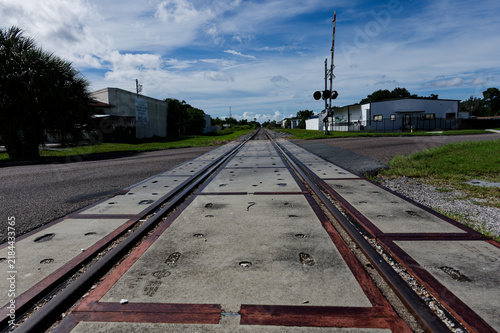Low-angle photo of rusty train tracks stretching into the distance across gravel and wooden sleepers in a suburban St. Petersburg, FL green setting, suggesting travel, solitude, perspective, industria