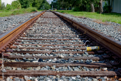 Low-angle photo of rusty train tracks stretching into the distance across gravel and wooden sleepers in a suburban St. Petersburg, FL green setting, suggesting travel, solitude, perspective, industria