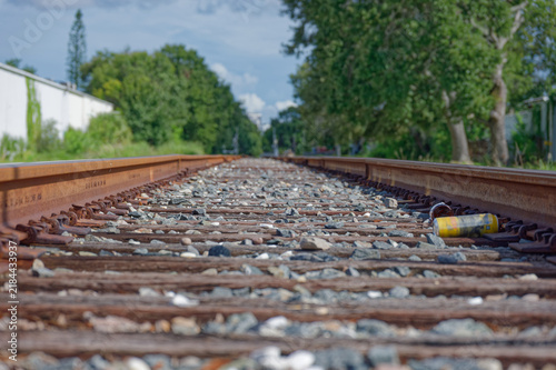 Low-angle photo of rusty train tracks stretching into the distance across gravel and wooden sleepers in a suburban St. Petersburg, FL green setting, suggesting travel, solitude, perspective, industria