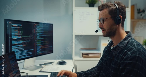 Young Caucasian male technical support specialist wearing headset speaks on computer at office. Professional call center help desk, Cyber security operator service, Online client consultation concept.