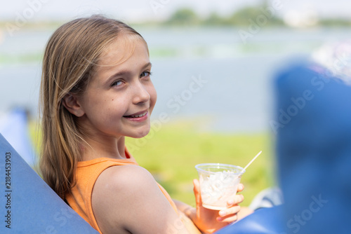 Bild auf Leinwand Smiling girl relaxing on a lounge chair while eating ice cream near a lake