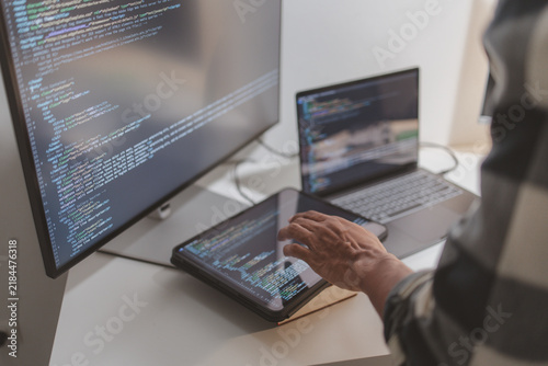 Software developer coding on laptop and tablet in a modern workspace. Close-up of programming workflow, software engineering, debugging source code, and multi-device application development.