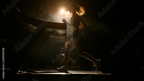 Workout, girl and running on treadmill in gym at night for fitness training, endurance challenge and calorie burning. Flare, late exercise and girl with breathing for intense cardio and race practice