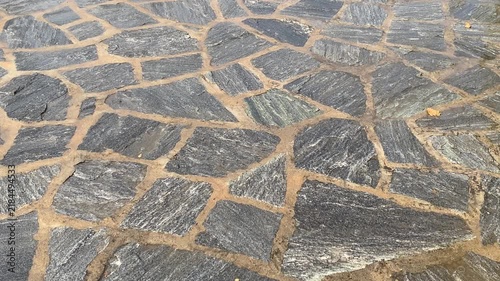 Rain falling on grey irregular flagstones set in light brown mortar.