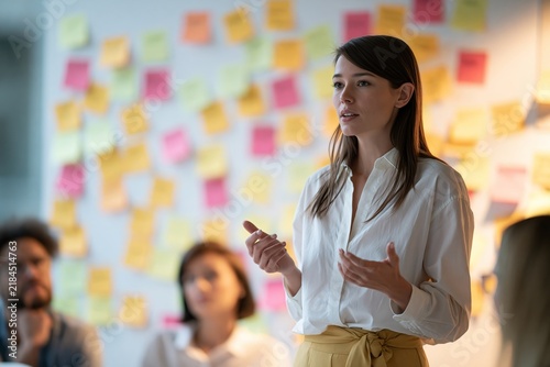 Young woman presenting ideas to her team in a creative office space with sticky notes on wall