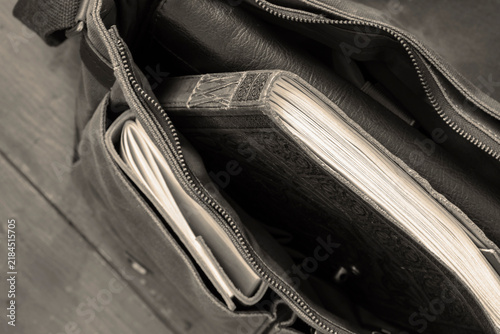 Green vintage style canvas messenger bag satchel, with a leather journal and clack folder. On a wooden floor background.