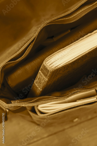 Green vintage style canvas messenger bag satchel, with a leather journal and clack folder. On a wooden floor background.