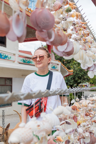 Fotografía Woman tourist browsing handmade seashell wind chimes and souvenirs at an outdoor local market in Thailand, representing travel, souvenir shopping, local crafts and coastal culture