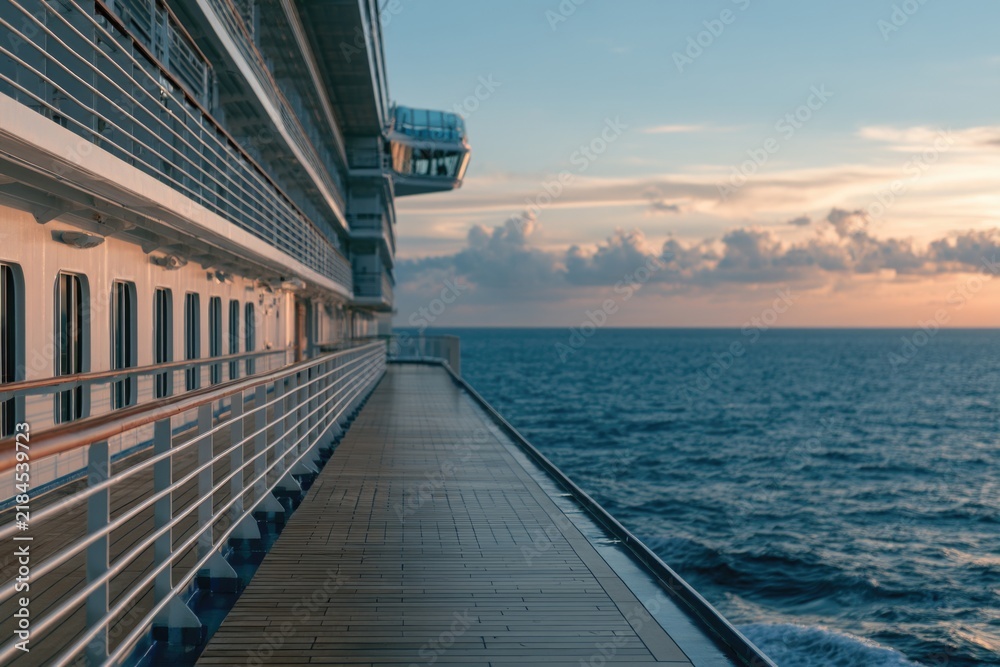 Obraz premium A cruise ship deck overlooking a calm ocean at sunset with soft clouds and warm light reflecting on the water.
