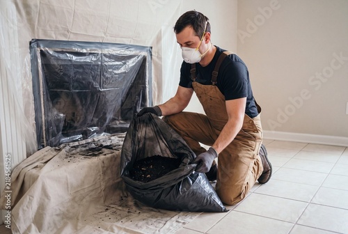 Professional removing fireplace ash into waste bag