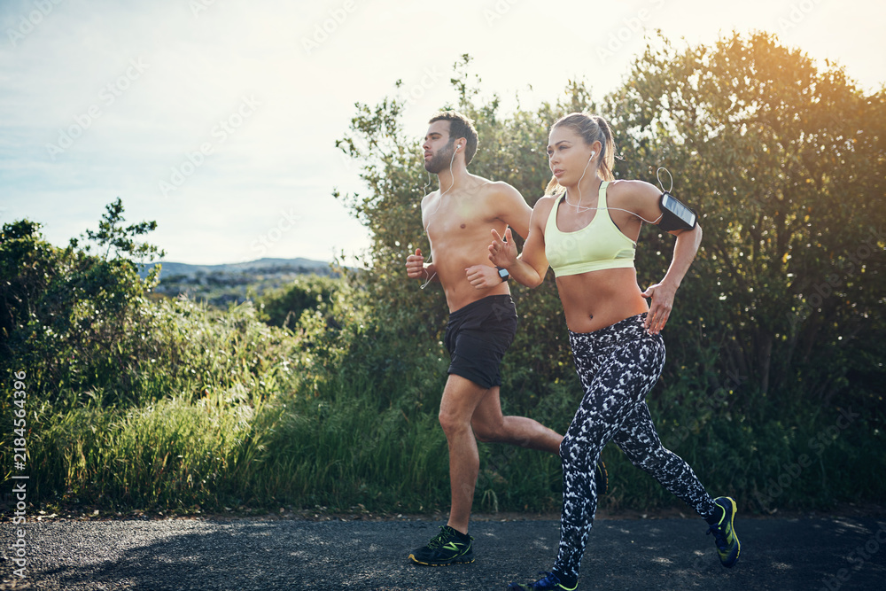 Obraz premium Fitness, couple or running with earphones on road for outdoor workout or cardio exercise together. Active, man and woman with sunshine or music for mountain challenge, health or wellness in nature